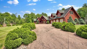 A large, red log cabin-style house with a driveway leading to a front porch.
