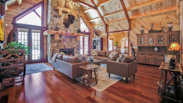 A spacious living room with a stone fireplace, wooden beams, and a high ceiling.