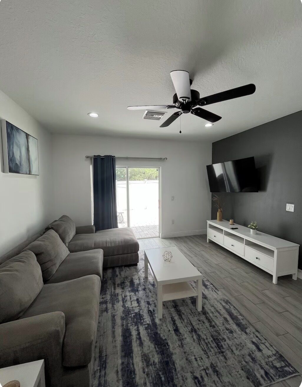 A modern living room with a sofa, a coffee table, a TV, and a ceiling fan.