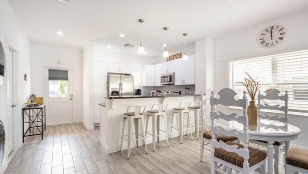 A modern kitchen with white cabinetry, a central island with bar stools, and a dining table with white chairs.