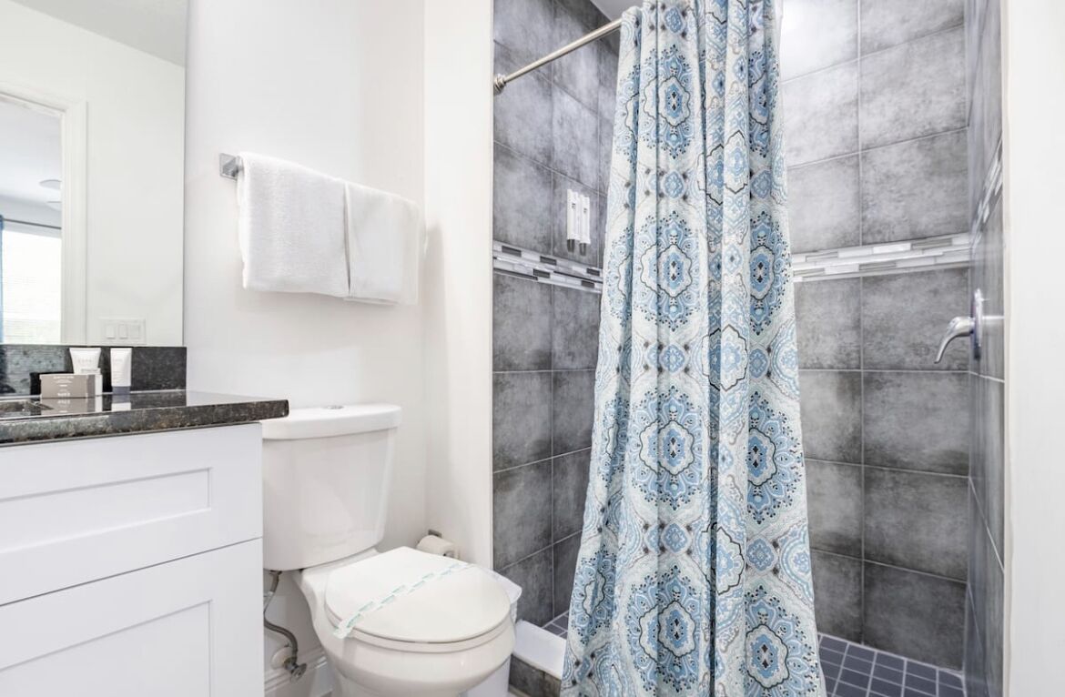 A bathroom with a white toilet, a white sink with a black countertop, and a shower with a patterned curtain.