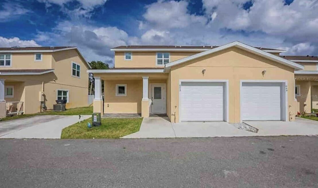 A two-story residential building with a beige exterior, a front driveway, and two garage doors.