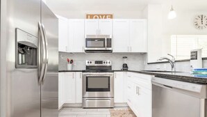 A modern kitchen with stainless steel appliances, white cabinetry, and a 'LOVE' sign above the microwave.