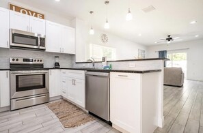 Una cocina moderna con muebles blancos, electrodomésticos de acero inoxidable e iluminación colgante.