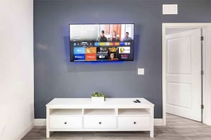 Un televisor de pantalla plana montado en una pared gris con un mueble bajo para entretenimiento blanco.