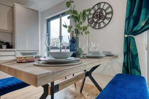 Un comedor con una mesa de madera, copas de vino, una botella y un reloj en la pared.