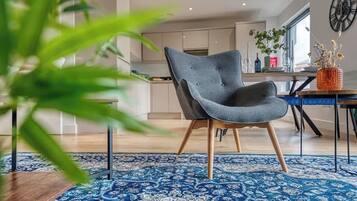 A modern living room with a blue patterned rug, a grey armchair, and a dining area with a blue table.