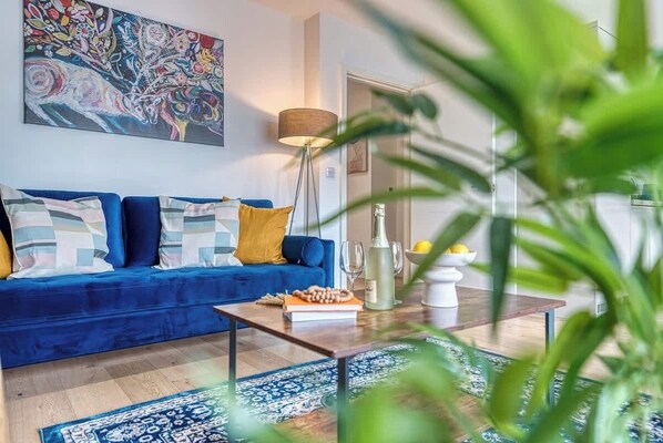 Ein Wohnzimmer mit blauem Sofa, einem Couchtisch, einer Lampe und einem Gemälde an der Wand.