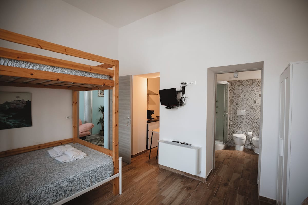Une pièce compacte comprenant un lit superposé, une petite kitchenette, une salle de bain avec douche et un téléviseur fixé au mur.