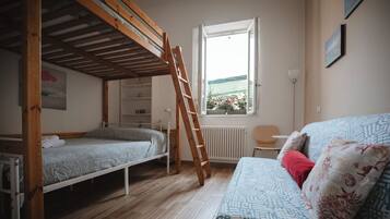 Et værelse med køjeseng, sofa, stige, et vindue med udsigt til planter og en radiator.