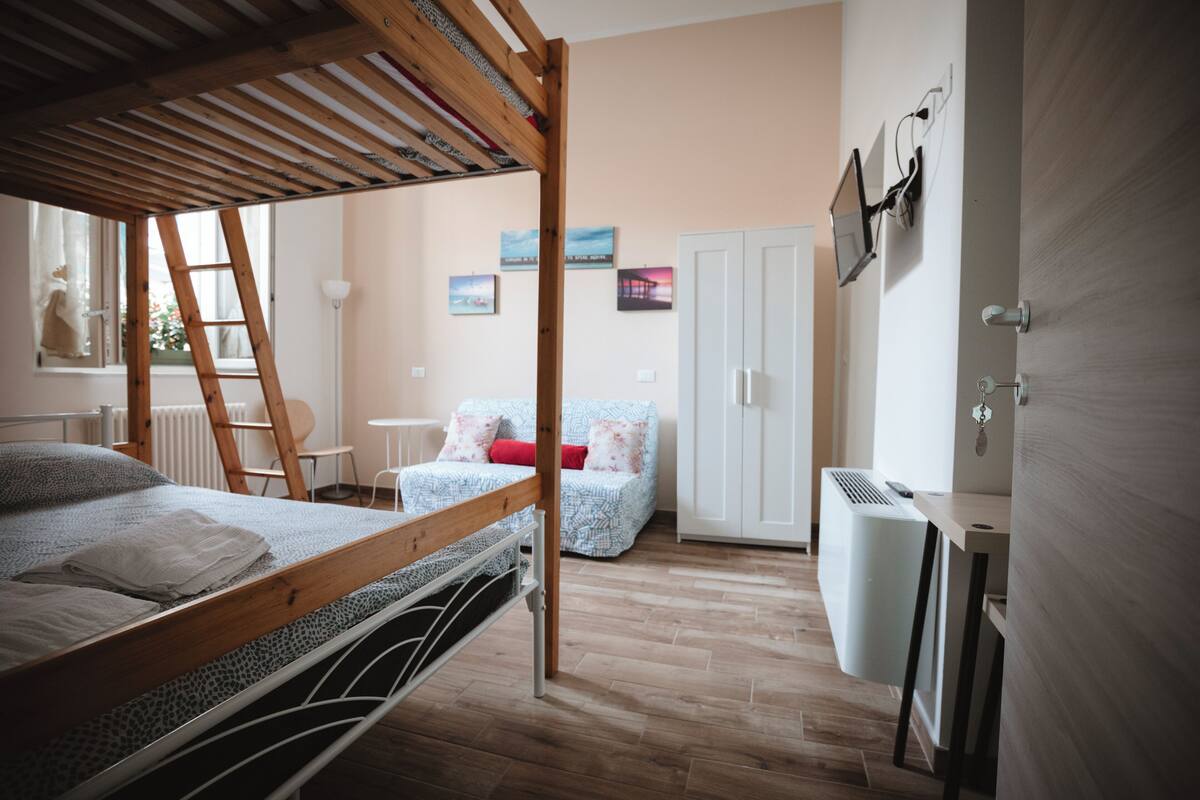 Une chambre avec un lit superposé, un bureau, un radiateur et une armoire.