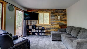 Ein gemütliches Wohnzimmer mit Steinwand, einem Wand-Fernseher, einem Ledersofa und einem Bücherregal.