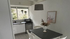 A kitchen with white cabinets, a black countertop, and a window with hanging plants. There is a dining table with white chairs and a vase with flowers. - Lake Garda Tignale vacation home bungalow with pool and lake view (Aer)