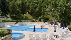 A swimming pool with lounge chairs and umbrellas, surrounded by greenery and a hillside. - Lake Garda Tignale vacation home bungalow with pool and lake view (Aer)