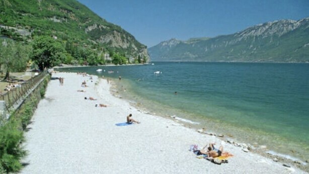 A beach with clear water, a sandy shore, and mountains in the background. - Lake Garda Tignale vacation home bungalow with pool and lake view (Aer)