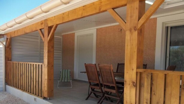 Un patio couvert doté d’une terrasse en bois, d’une table avec des chaises et d’une porte-fenêtre coulissante donnant sur une pièce intérieure.