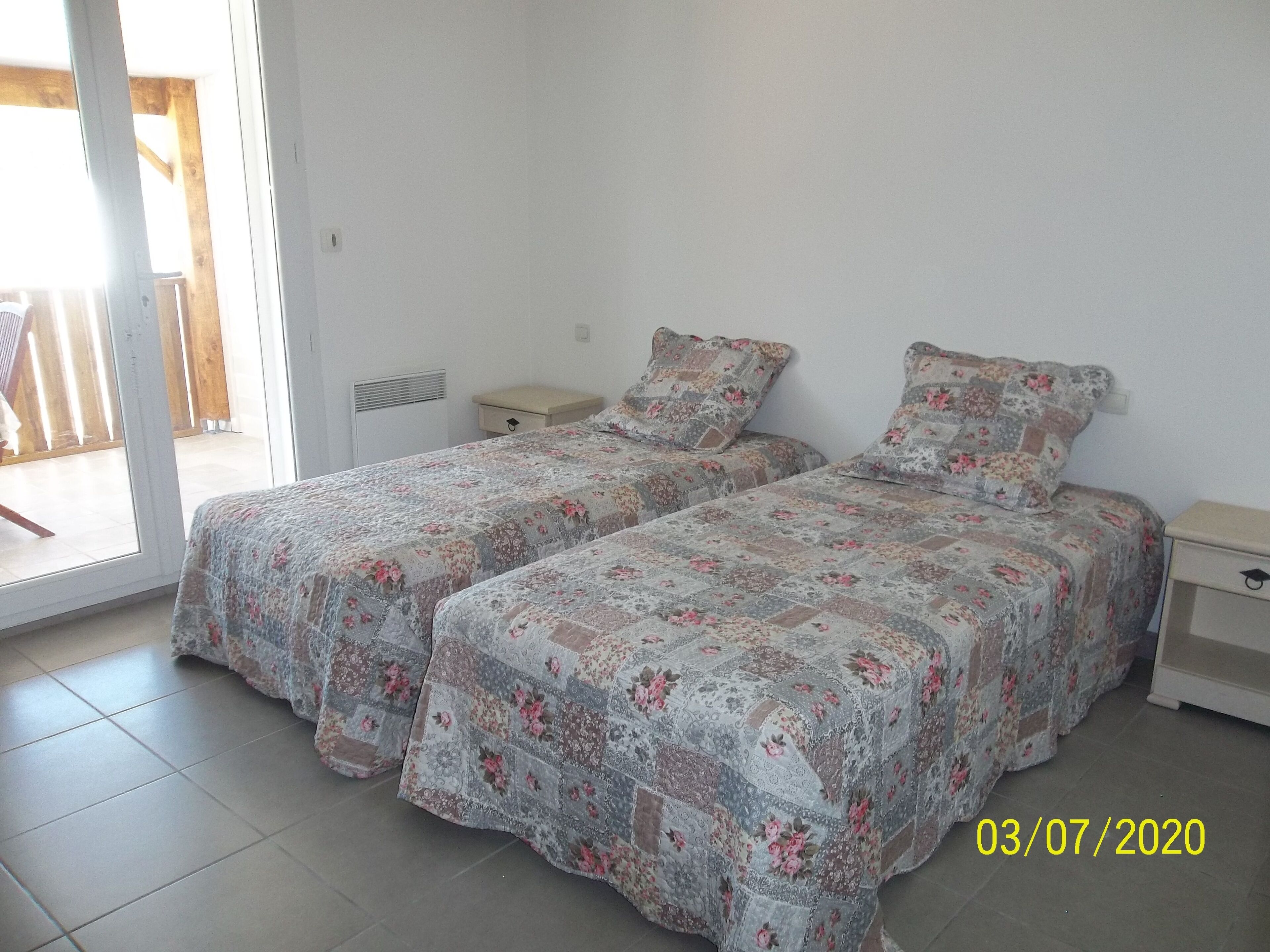 Ein Zimmer mit zwei Betten, einem kleinen Nachttisch, einem Beistelltisch und einer Schiebetür zu einem Außenbereich.