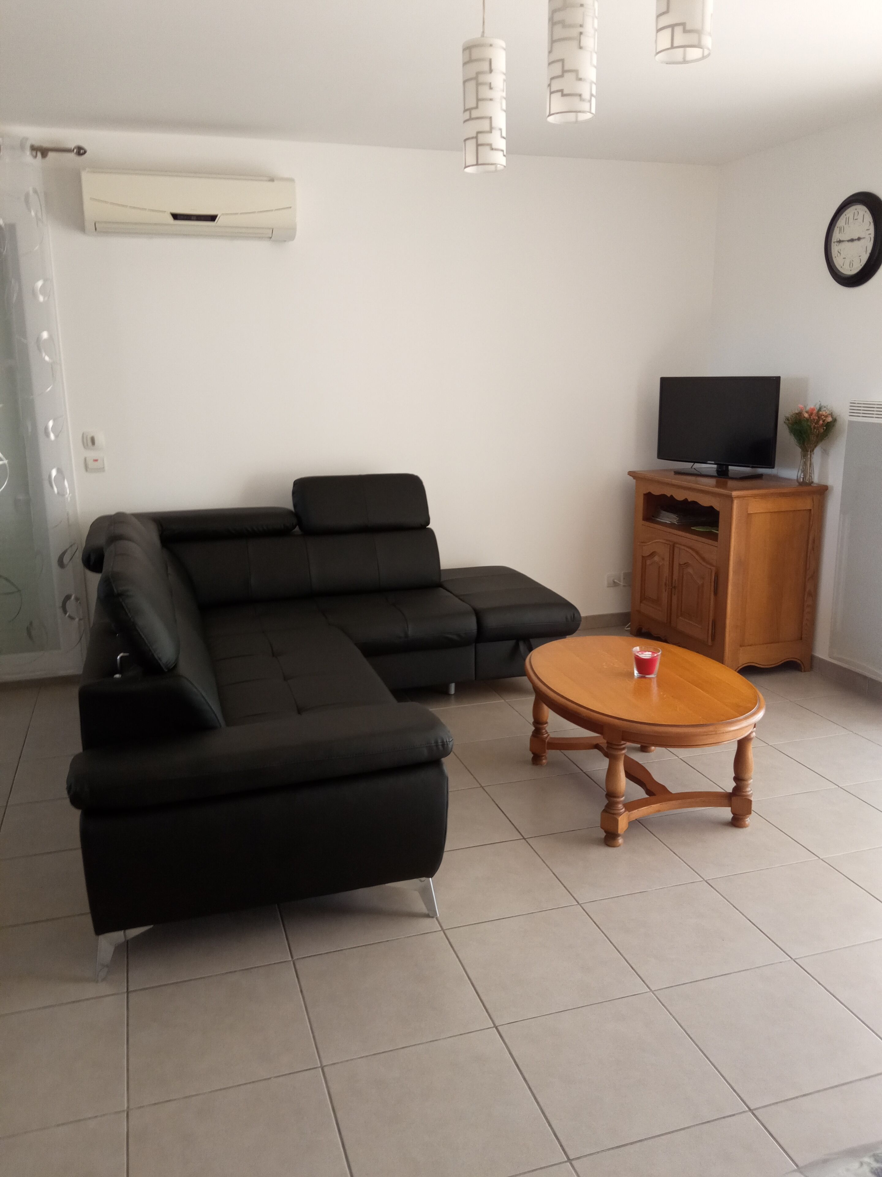 Een moderne woonkamer met een zwarte modulaire bank, een houten salontafel, een televisie op een houten kast, en een wandairconditioning.