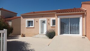 Une maison à deux étages, avec un toit recouvert de tuiles rouges, une porte d’entrée et une grande porte-fenêtre coulissante.