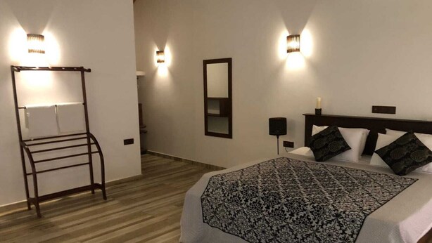 A bedroom with a bed, a nightstand, a wall-mounted mirror, and a wooden floor. - Namaste Nilaveli (Nilaveli)