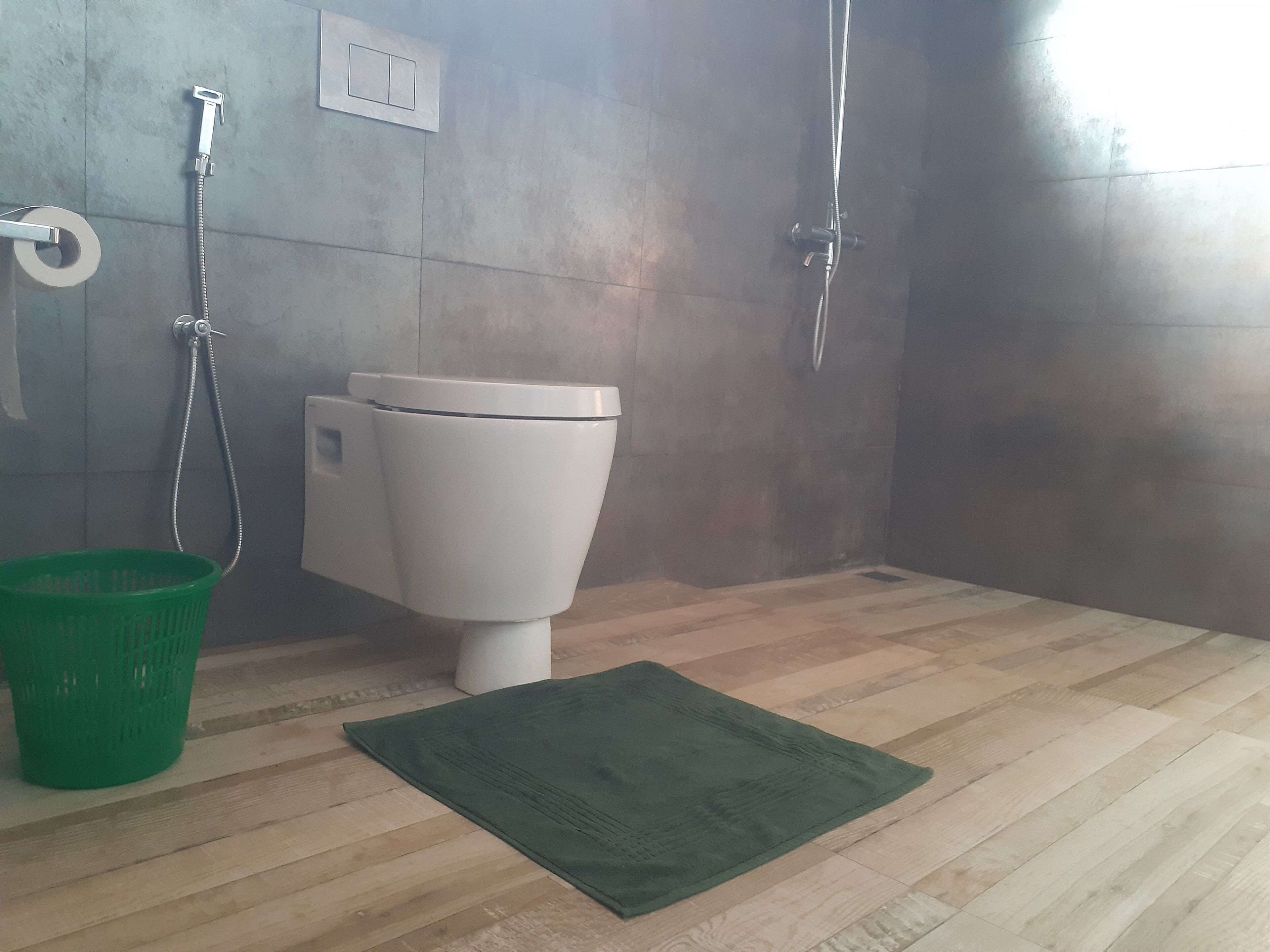 A bathroom with a toilet, a green basket, and a shower area.