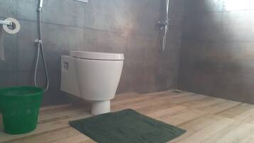 A bathroom with a toilet, a green basket, and a shower area.
