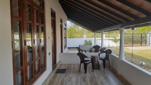 A covered patio with a wooden ceiling, a table with chairs, and large windows with wooden frames. - Namaste Nilaveli (Nilaveli)