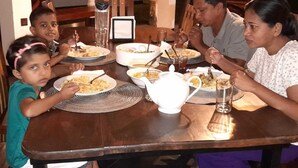 A family dining at a wooden table with plates of food, glasses, and a teapot. - Namaste Nilaveli (Nilaveli)