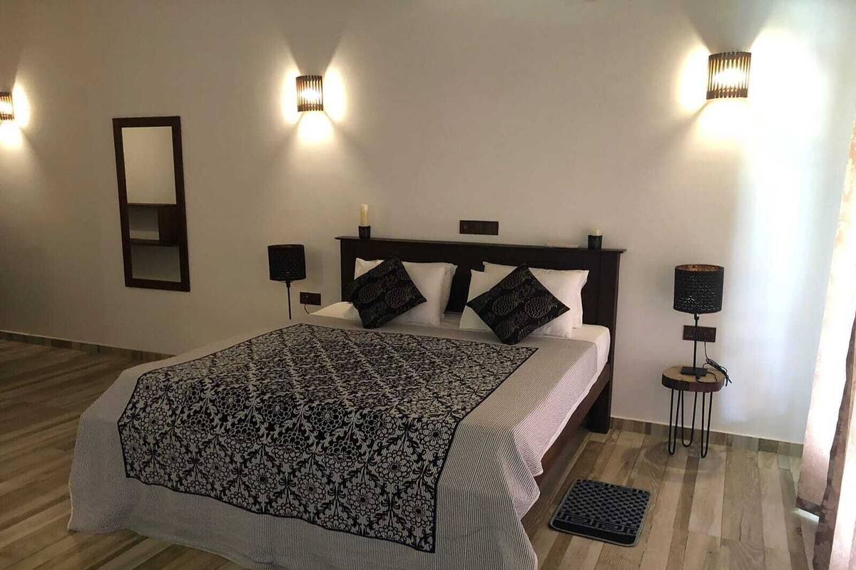 Ein Schlafzimmer mit Bett, Nachttischlampen, einem Nachttisch, einem Spiegel und einer Stehlampe.