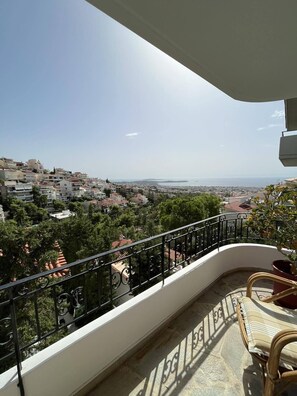 A balcony with a view of a coastal town, a chair, and a potted plant. - Studio with breathtaking view (Voula)