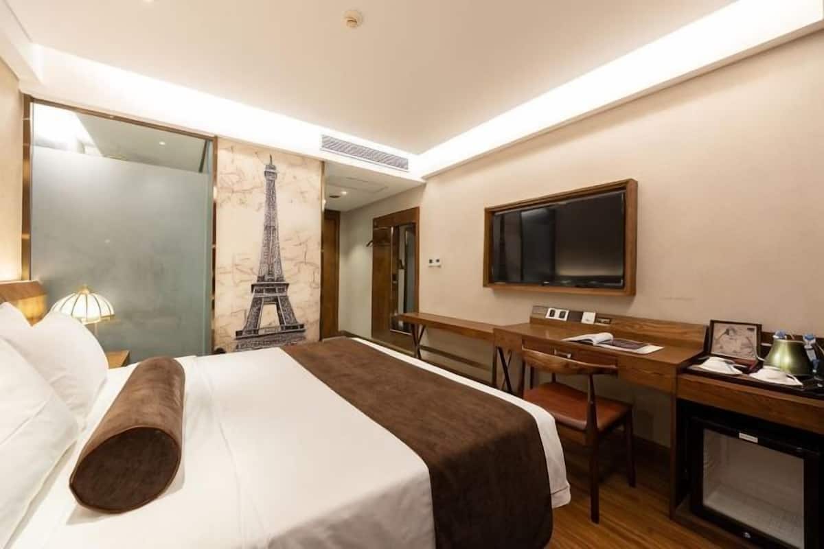 Ein Hotelzimmer mit Bett, Schreibtisch, Stuhl, Fernseher und einer dekorativen Eiffelturm-Darstellung an der Wand.