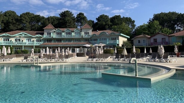 Una piscina con sillas de descanso y sombrillas, rodeada de edificios con balcones.
