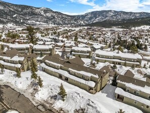 Un barrio residencial cubierto de nieve con varias casas de dos pisos, cielo despejado y montañas al fondo.