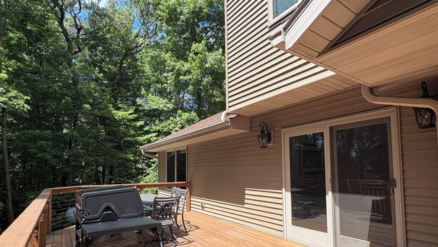A deck with a grill and outdoor furniture, a sliding glass door, and a view of a forested area. - Quiet relaxing wooded property. (New London)