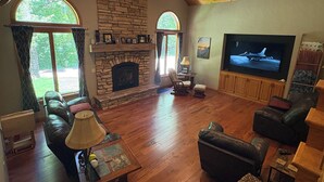 A living room with a stone fireplace, leather sofas, a television, and wooden flooring. - Quiet relaxing wooded property. (New London)