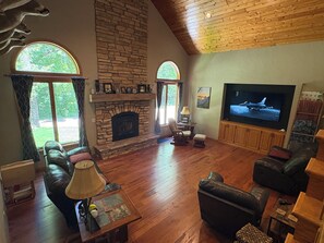 A living room with a stone fireplace, leather sofas, a television, and wooden flooring.