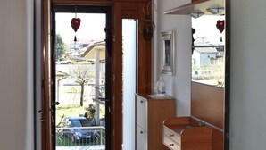 A hallway with a wooden door leading to a balcony, a white and yellow ceiling, and a small kitchen area with a sink and cabinets. - Sundial One. Pradamano (Pradamano)