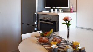 A modern kitchen with a refrigerator, oven, and microwave. There is a dining table with breakfast items and a vase with a flower. - Sundial One. Pradamano (Pradamano)