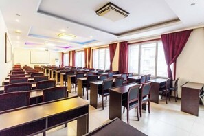 Une salle de conférence avec des rangées de tables et de chaises, un pupitre et de grandes fenêtres équipées de rideaux.