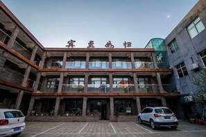 A multi-story building with a central entrance, a parking area with cars, and a clear sky. - Yesanpo Hostel (Laishui)