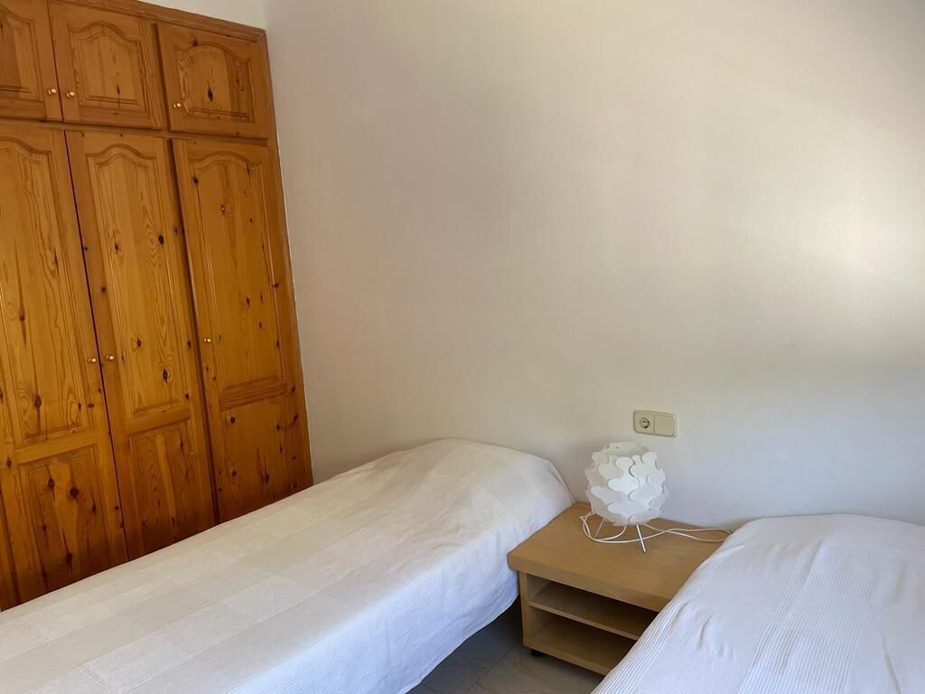 Un dormitorio con dos camas individuales, un armario de madera y una mesita de noche con una lámpara decorativa.