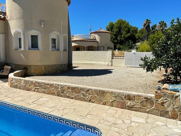 A pool area with stone tiles, a building with arched windows, and a clear blue sky.