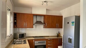 A kitchen with wooden cabinets, a stainless steel refrigerator, a microwave, an oven, and a sink.