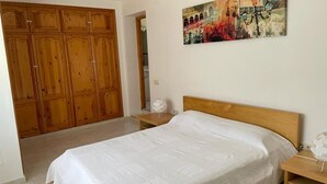 A bedroom with a large bed, wooden wardrobe, and a painting on the wall.