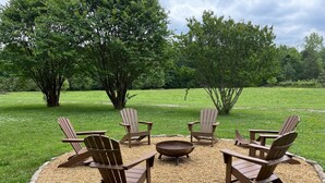 Un espace extérieur circulaire aménagé avec des chaises Adirondack et un foyer, entouré d’une bordure de gravier et d’une pelouse.