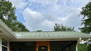 Une maison en bois avec un toit vert, un porche à l’avant et des fondations en briques.