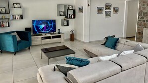 Een moderne woonkamer met een flatscreen televisie, teal- en grijze banken, een bijzettafeltje en een boekenkast.