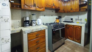 Une cuisine avec des meubles de rangement en bois, une cuisinière à gaz, une machine à café et un mixeur.