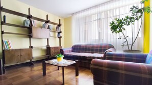 Un salon avec un canapé, des fauteuils, une table basse, une bibliothèque et une plante en pot.