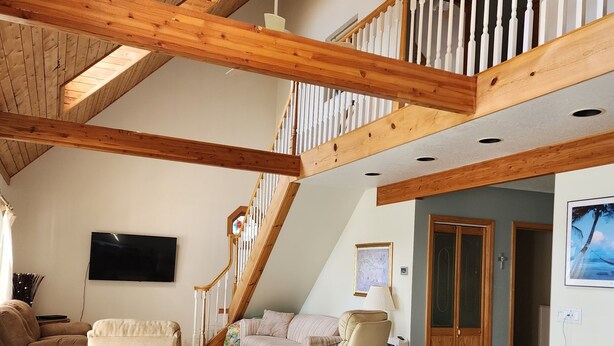 A spacious living area with a high ceiling, wooden beams, a staircase, a flat-screen TV, and a dining table with chairs. - The Cottage at Hubbard Lake (Hubbard Lake)